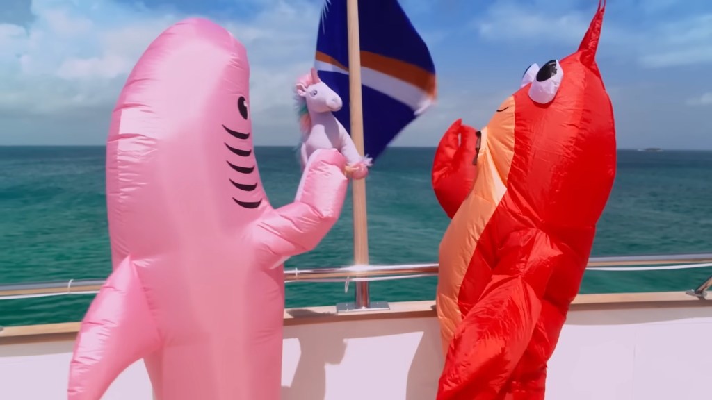 Meredith Marks in a pink inflatable Shark costume throwing a purple unicorn into the ocean, while standing next to Bronwyn Newport, in a red lobster costume