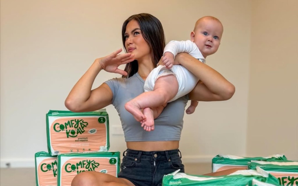 Gael Cameron holding up her baby and sitting amongst a bunch of diaper boxes