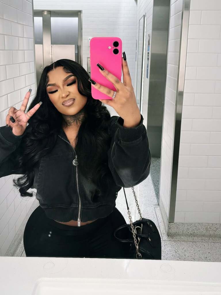 Erica Banks in a black jacket taking a selfie in a bathroom