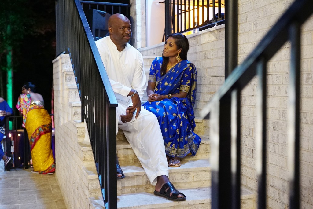 Dr. Jackie Walters in a blue dress sitting outside on a staricase and looking at Curtis Berry dressed in all white