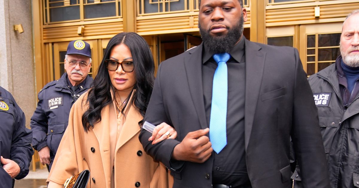 Jen Shah in a brown coat walking arm in arm with a security guard, leaving a courthouse