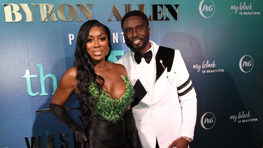 Wendy Osefo in a green and black gown standing with Eddie Osefo in a white suit