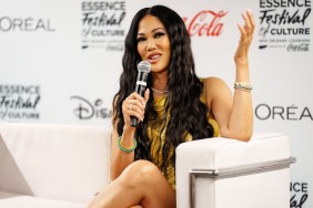 Kimora Lee Simmons in a gold dress sitting on stage holding a microphone and her hand