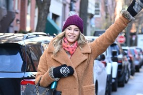 Meghan King in a brown coat and mittens walking down the street and waving