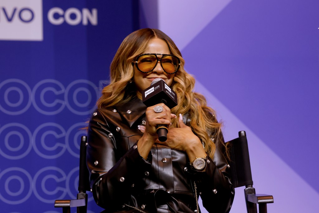 Mary Cosby in a black leather jacket on stage at BravoCon 2025, holding a microphone and smiling
