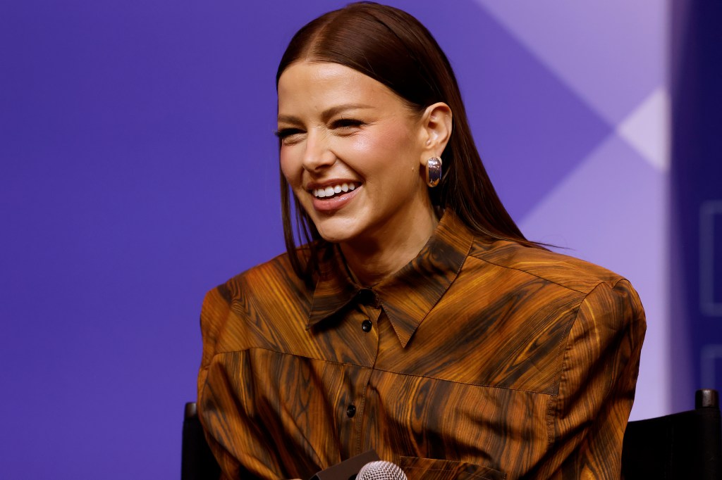 Ariana Madix in an orange shirt, smiling on stage at BravoCon