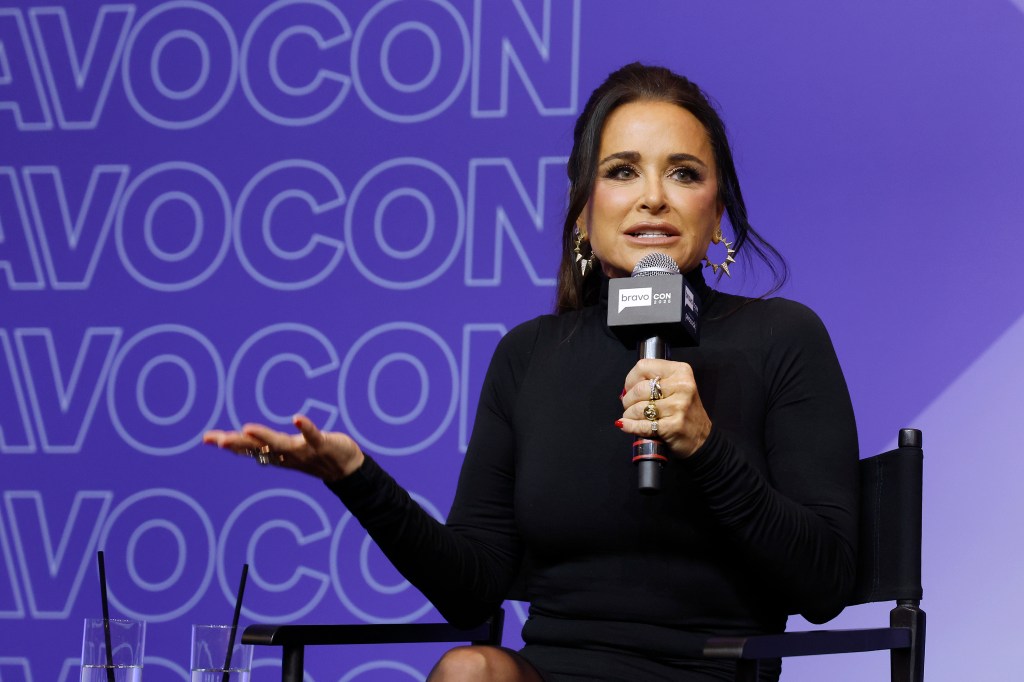 Kyle Richards in a black sweater holding her hand out and talking into a microphone at BravoCon 2025