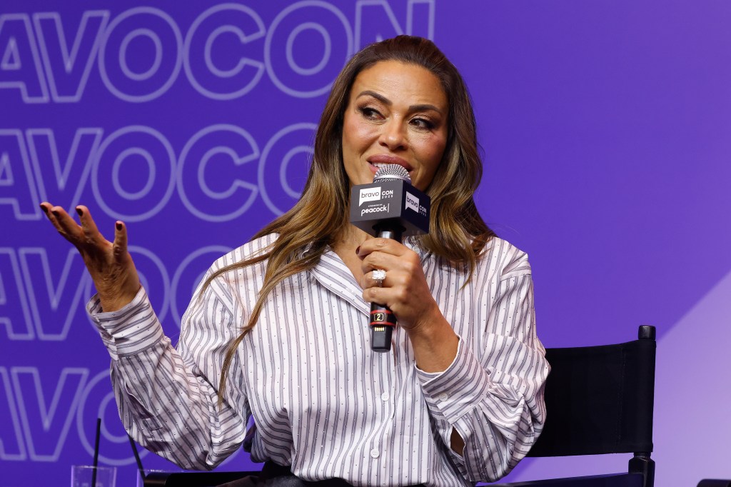 Dolores Catania on stage at BravoCon 2025, holding her hand out with a microphone