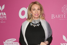 Lea Black posing on a red carpet in a black dress with a large silver necklace