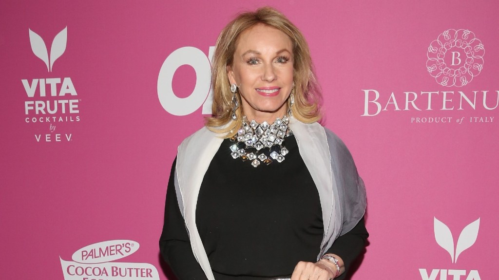Lea Black posing on a red carpet in a black dress with a large silver necklace