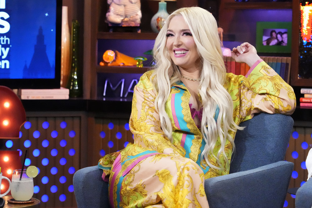 Erika Jayne in a yellow jumpsuit leaning back in her chair and grinning on Watch What Happens Live