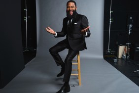 Anthony Anderson sitting on a wooden stool, wearing a black suit
