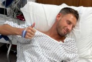 Fraser Olender laying in a hospital bed giving a thumbs-up to the camera
