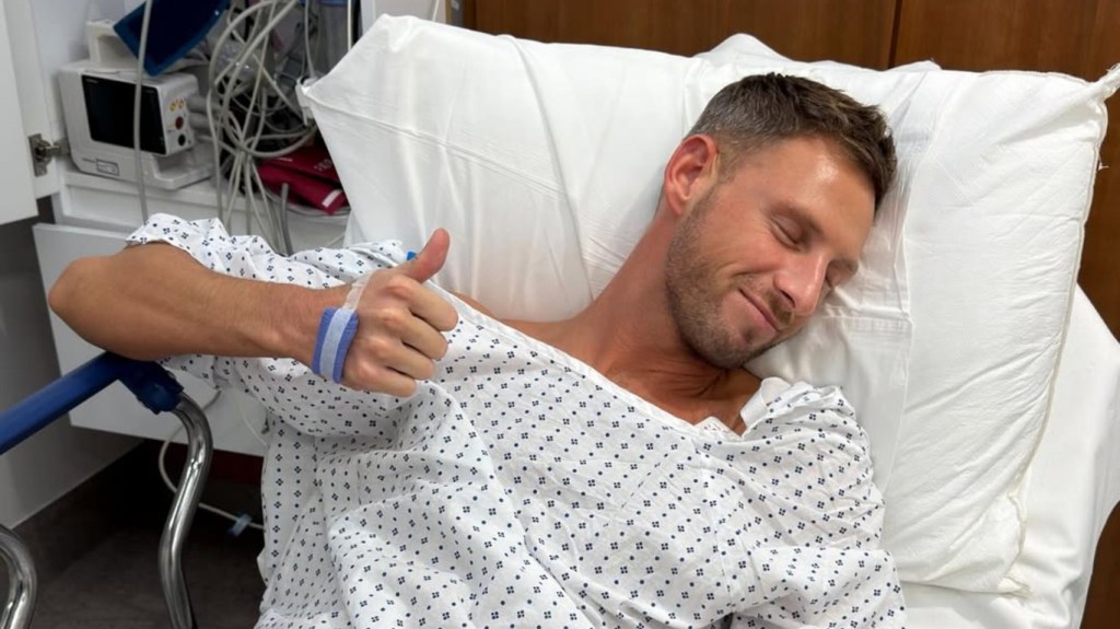 Fraser Olender laying in a hospital bed giving a thumbs-up to the camera