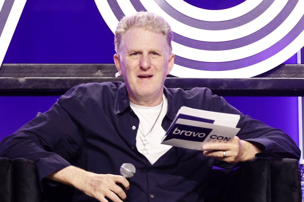 Michael Rapaport on stage at BravoCon 2023 holding cards and a microphone