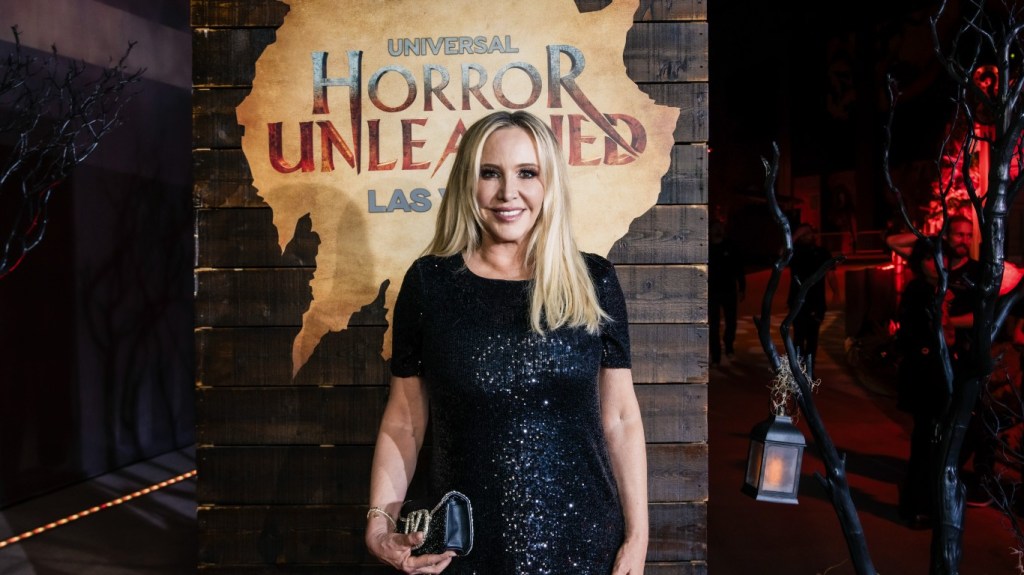 Shannon Beador in a black dress standing in front of a sign that says, "Horror Unleashed"