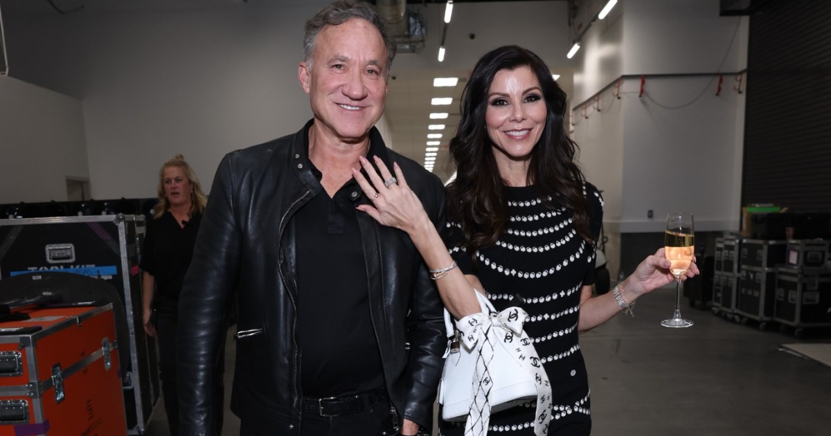 Terry Dubrow and Heather Dubrow walking arm in arm backstage at BravoCon, Heather has a glass of champagne