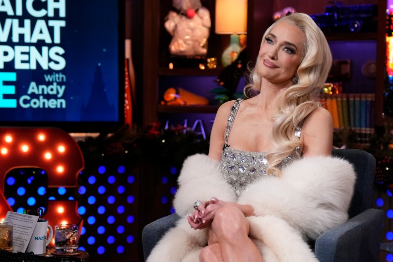 Erika Jayne wearing white fur and a silver dress, sitting with her legs crossed and smiling on Watch What Happens Live