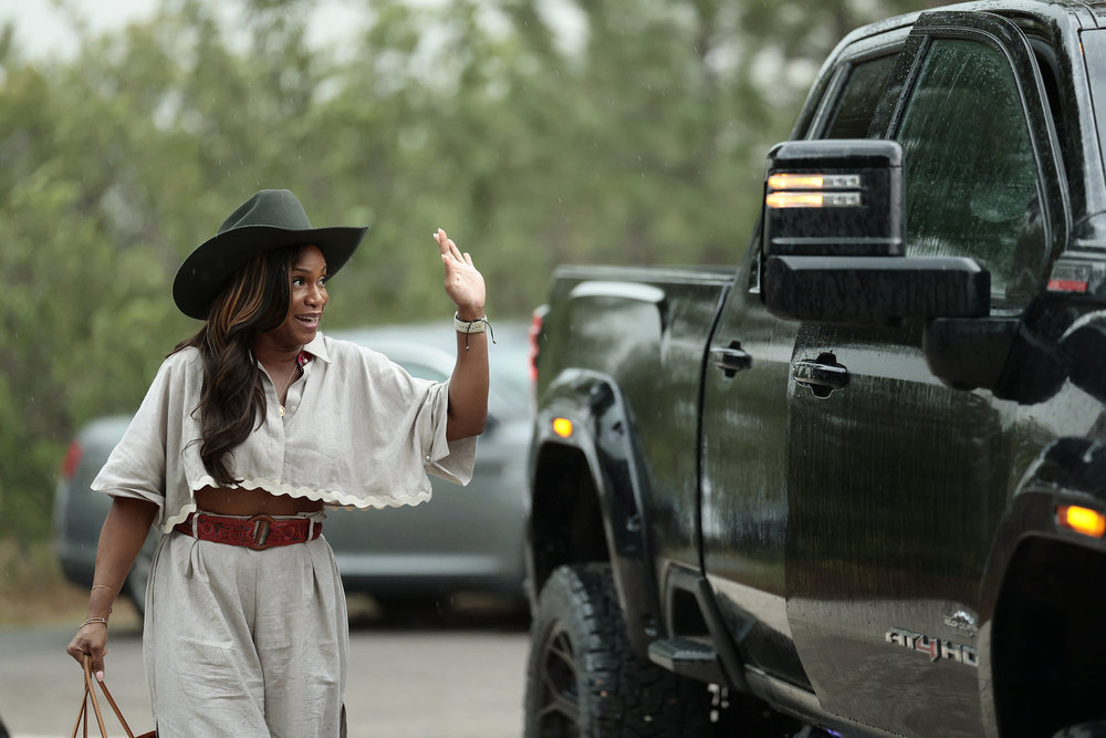 Tia Glover in a cowgirl hat, waving at a black truck