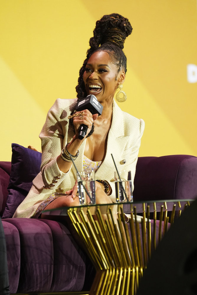 Monique Samuels on stage at BravoCon, laughing and holding a microphone 