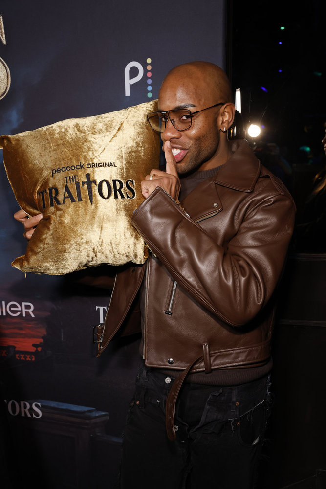 Monet X Change holding up pillow that says The Traitors  