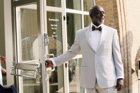 Peter Thomas holding open a door and waring a white suit