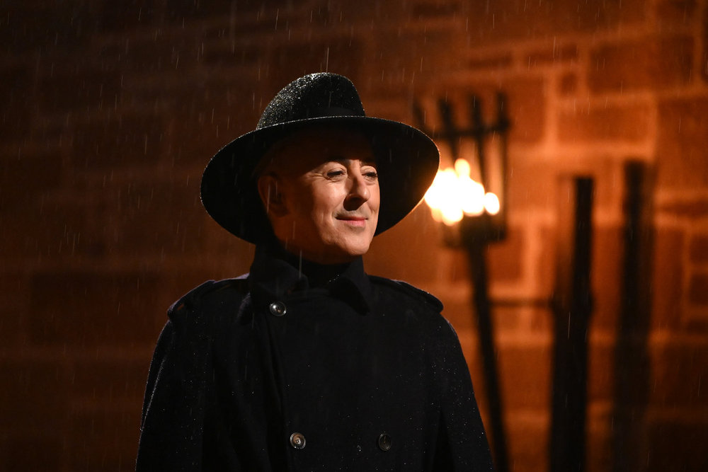 Alan Cumming in a black coat standing next to a torch on The Traitos Season 4 