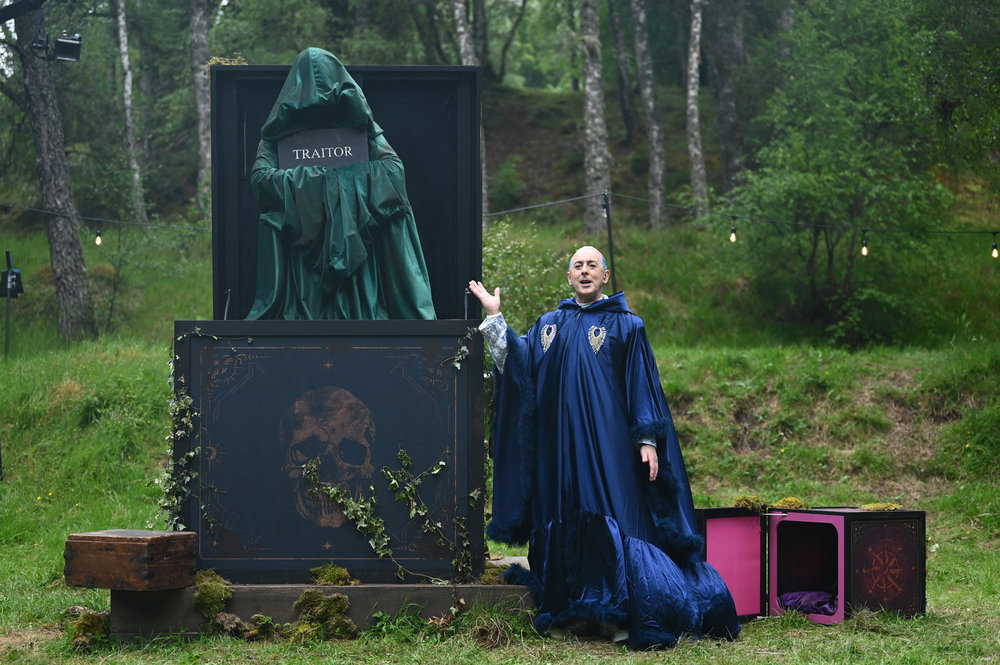 Alan Cumming standing next to a giant Traitor statue in Season 4 of The Traitors 