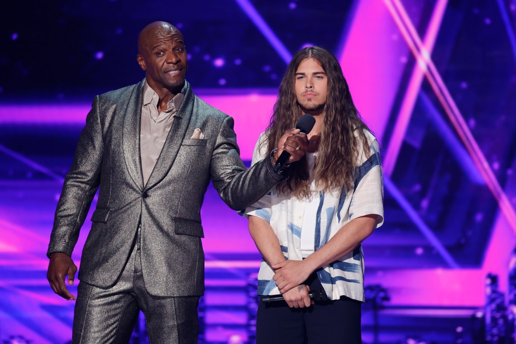 Terry Crews in a silver suit holding up a microphone to Jourdan Blue