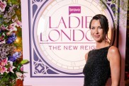 Margo Stilley in a black dress posing next to the Ladies of London logo