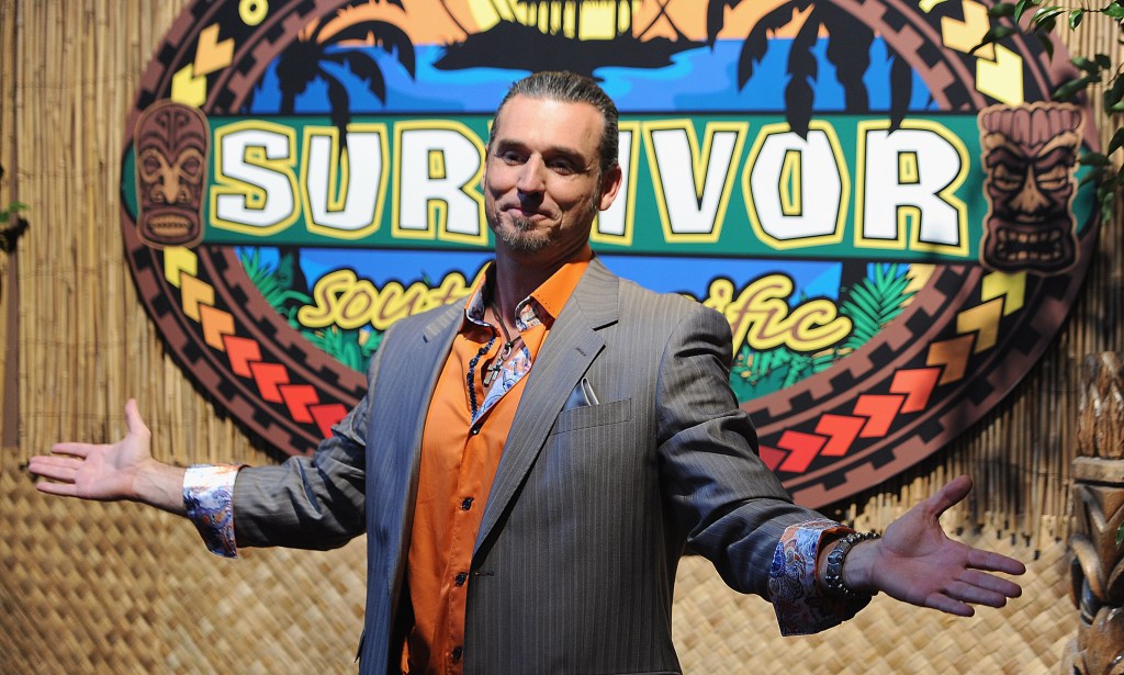Benjamin Coach Wade with his arms out in front of the Survivor logo