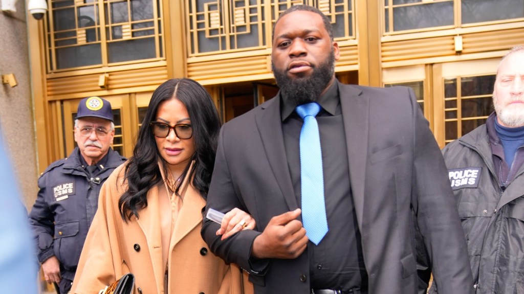 Jen Shah in a brown coat leaving court, locked arms with a man in a black suit