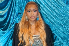 Drew Sidora in a silver top and black blazer posing in front of blue drapery