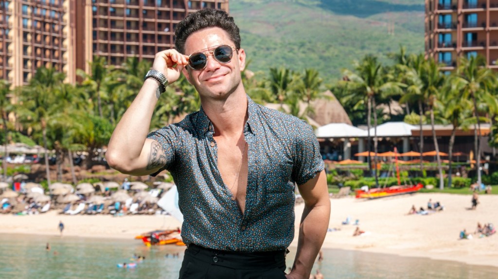 Sasha Farber posing in front of a beach wearing sunglasses