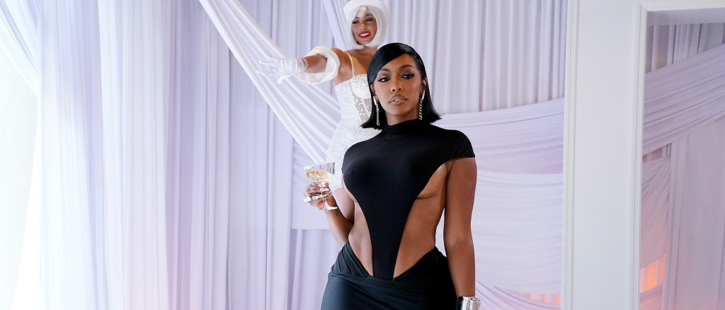 Porsha Williams in a black dress, surrounded by white drapes holding a a glass of champagne