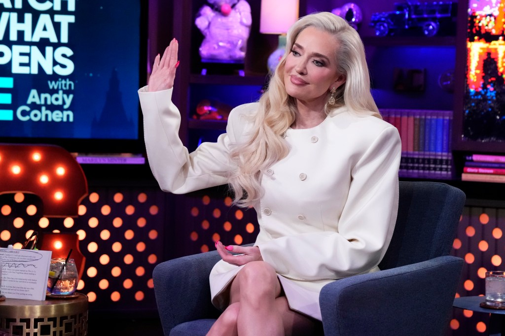Erika Jayne in a white dress raising her right hand on Watch What Happens Live