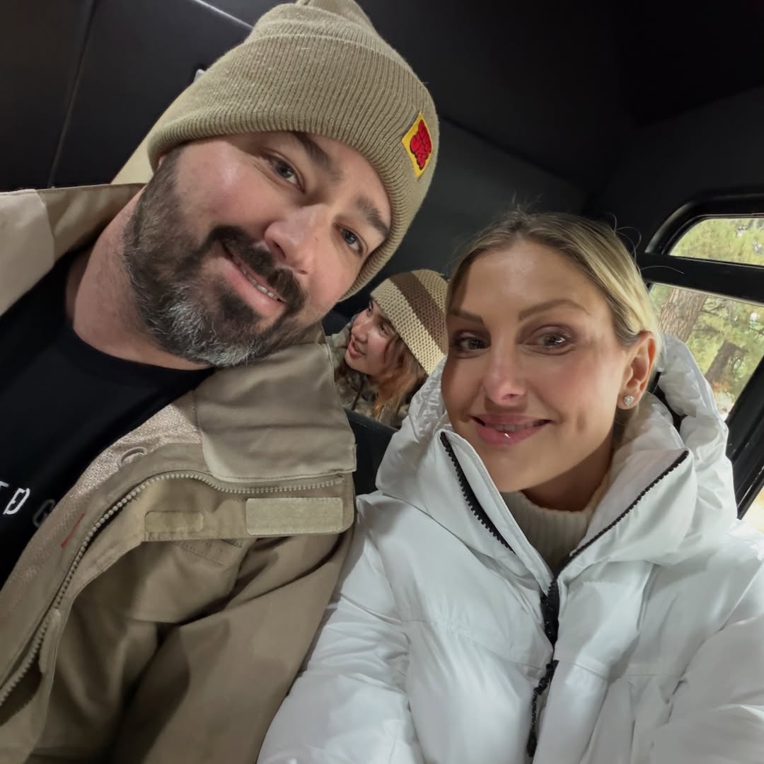 Gina Kirschenheiter and Travis Mullen posing in a car for a selfie, wearing coats and hats