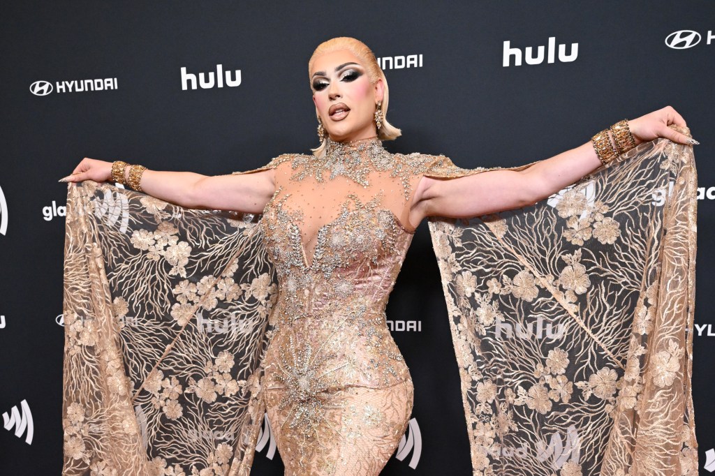 Plane Jane at the GLAAD Media Awards holding out a golden cape