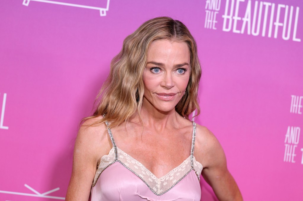 Denise Richards in a pink dress posing in front of a pink backdrop