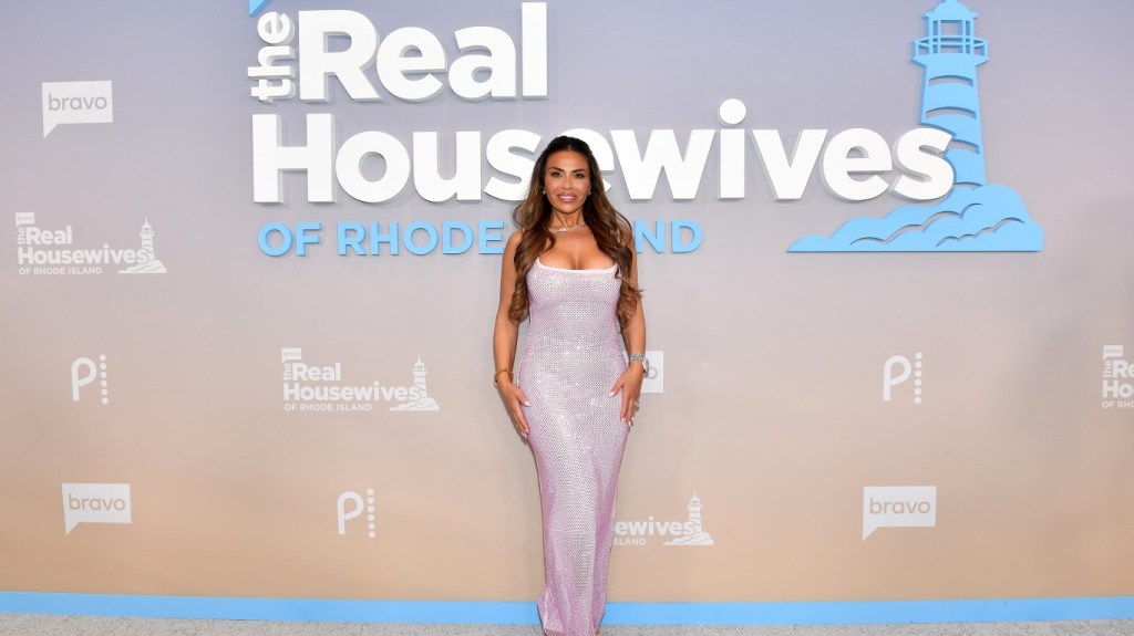 Dolores Catania posing in front of the Real Housewives of Rhode Island logo