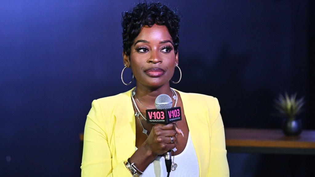Shamea Morton in a yellow blazer looking sideways and holding a microphone