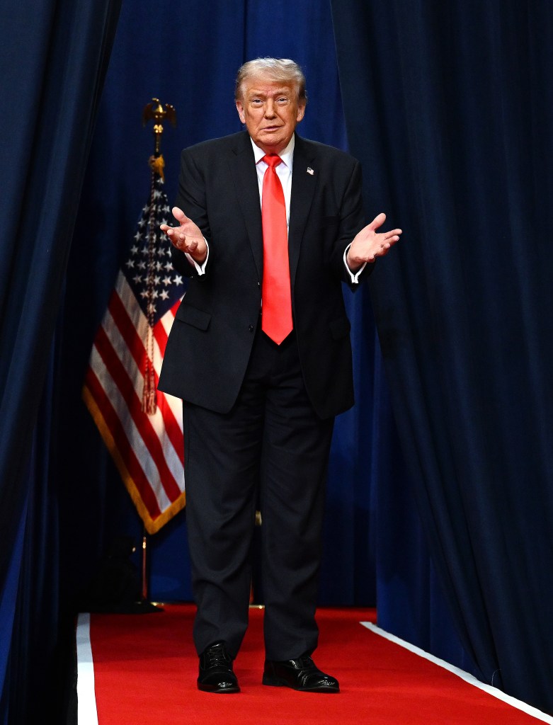 Donald Trump in a red tie standing with his hands out 