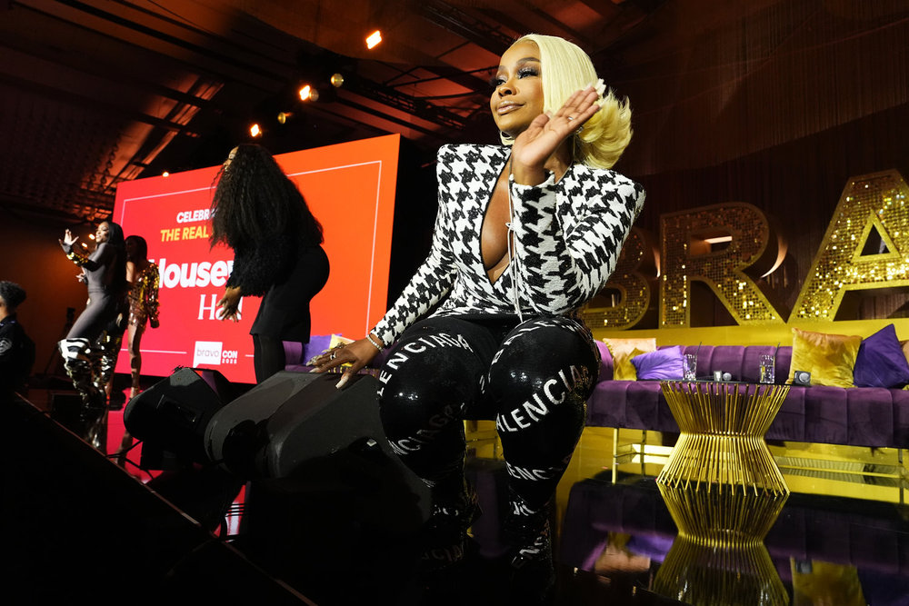 Phaedra Parks in a white and black houndstooth dress on stage at BravoCon squatting down towards the audience