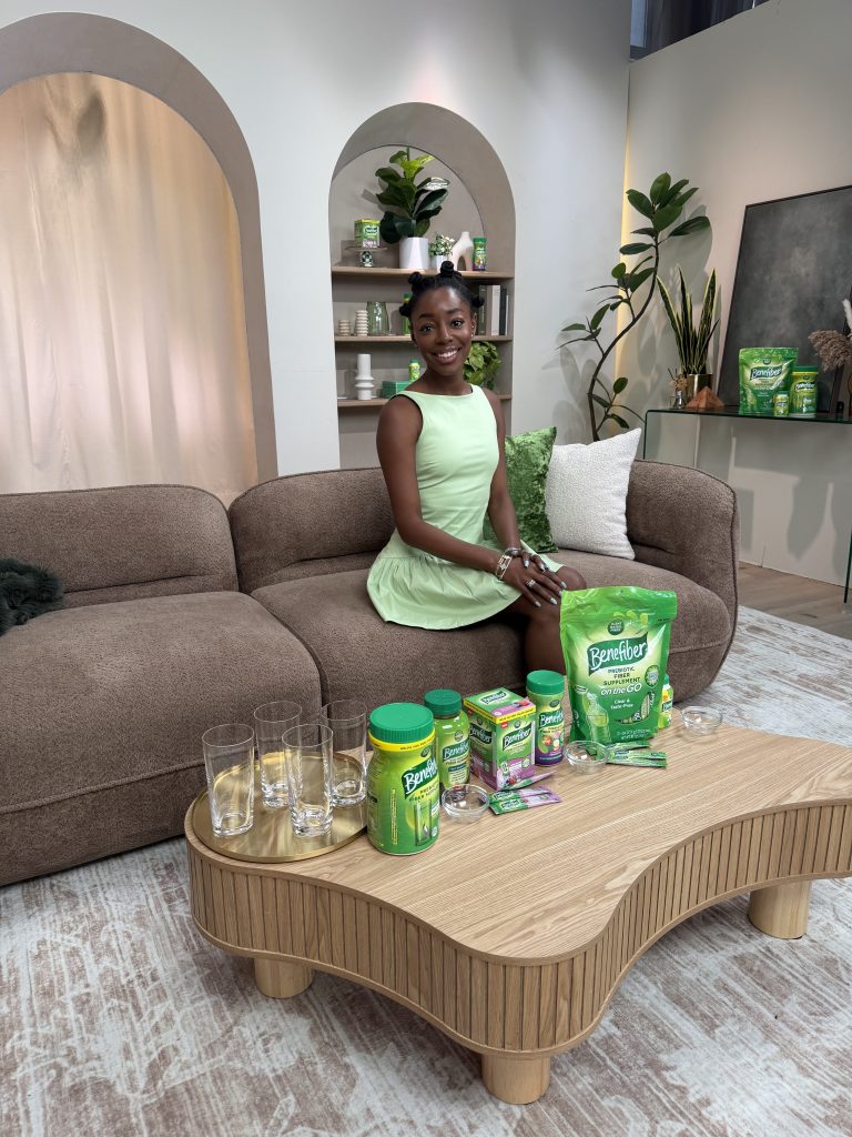 Venita Aspen in a green dress sitting on a couch surrounded by Benefiber products