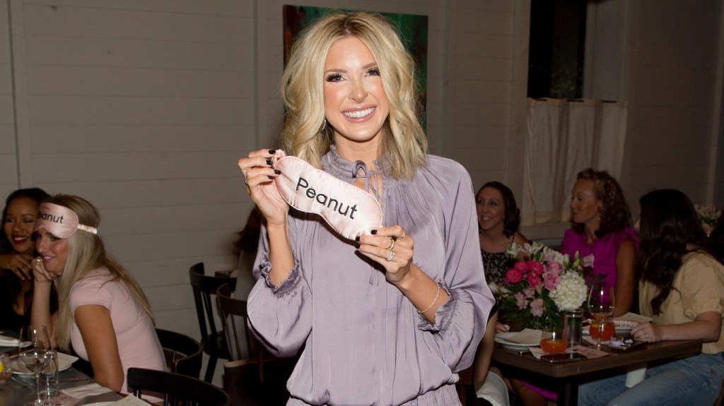 Lindsie Chrisley holding up an eye mask that says "peanut"