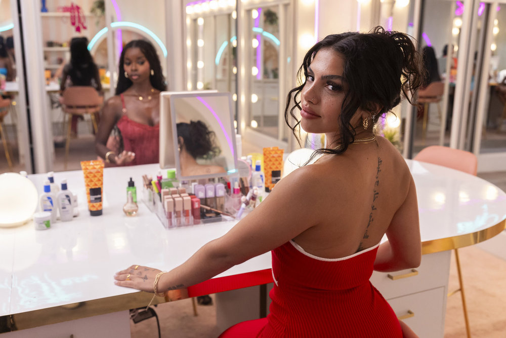 Huda Mustafa in a red dress looking over her shoulder sitting at a vanity on Love Island USA