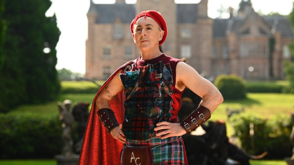 Alan Cumming in red tartan posing with his hands on his hips on The Traitors Season 4