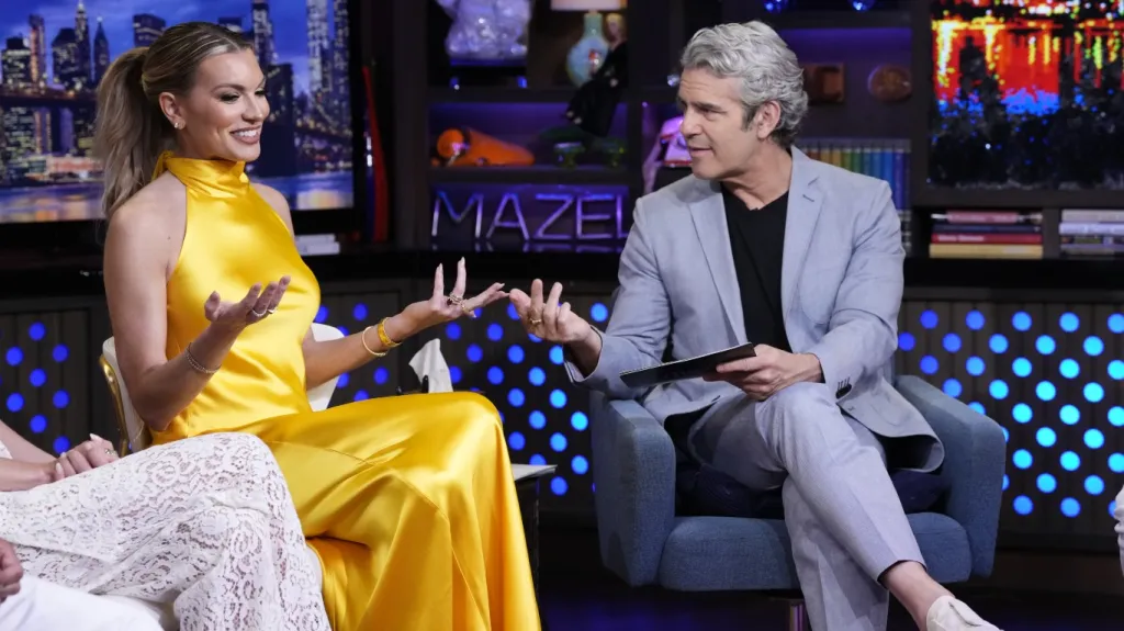 Lindsay Hubbard in a yellow dress in the Watch What Happens Live clubhouse with her hands out, facing Andy Cohen